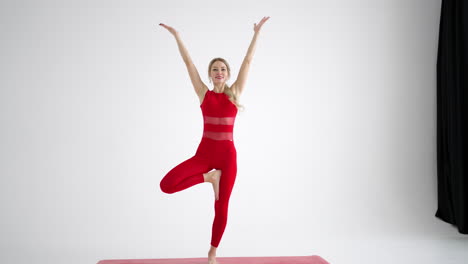 A-woman-in-a-red-tracksuit-looking-into-the-camera-conducts-training-and-tells-and-shows-exercises-from-yoga-or-Pilates-on-a-white-background.-Yoga-instructor-shows-exercises-for-home-classes